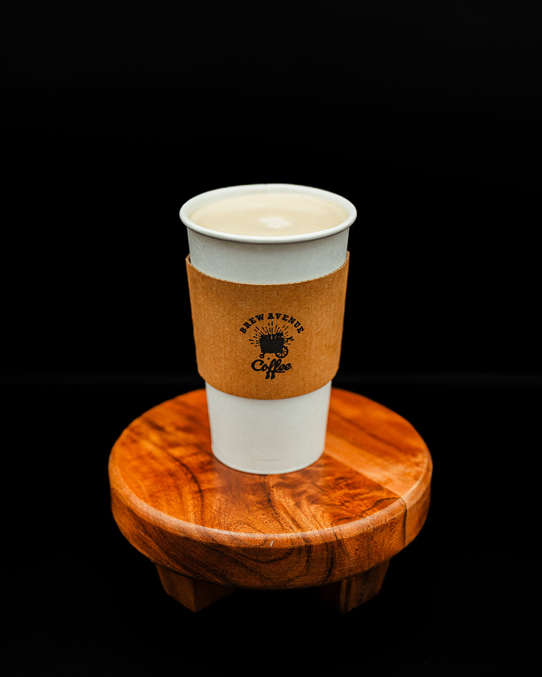 Cappuccino in a white cup with the Brew Avenue Coffee logo on a wooden stool.