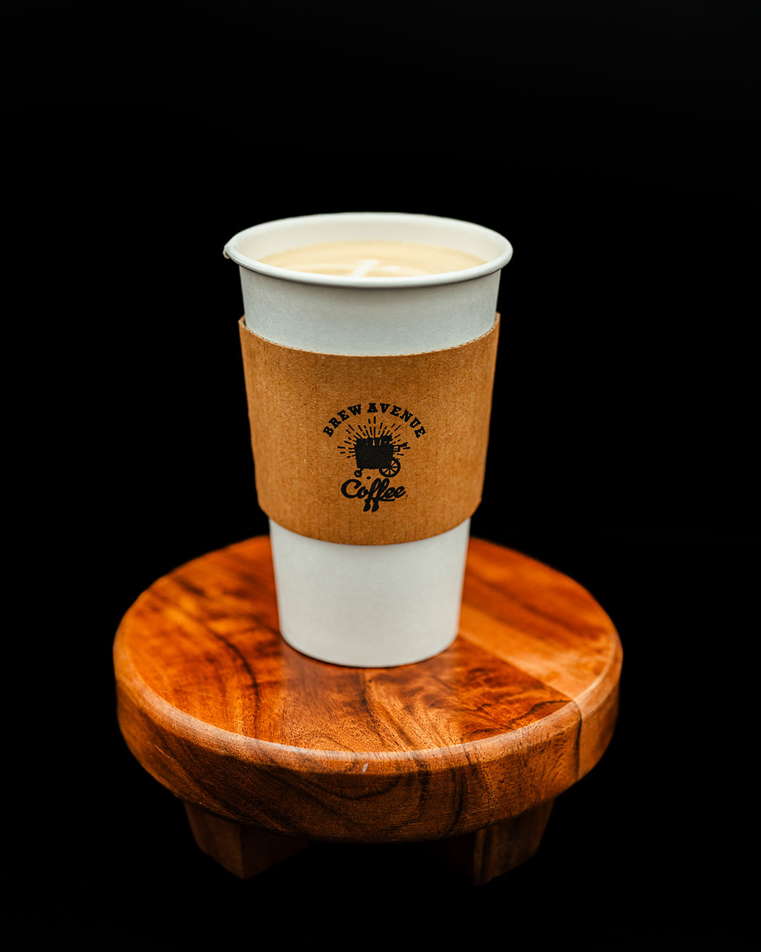 Latte in a white cup with the Brew Avenue Coffee logo on a wooden stool.